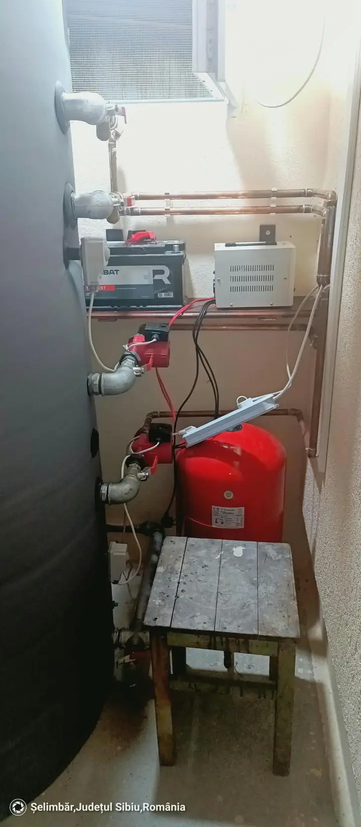 Rezervor mare de apă caldă, vas de expansiune roșu și pompe într-o magazie mică, în Șelimbăr