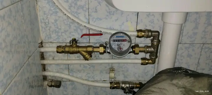 Contor de apă cu robineți de alamă și țevi albe pe un perete de baie